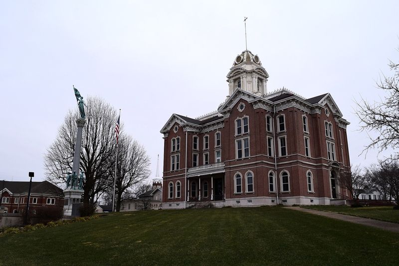 The red brick Posey County Courthouse with a white cupola, beside a tall memorial column on the courthouse lawn