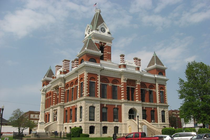 The Gibson County Courthouse, a red brick and limestone building with a tall clock tower and corner turrets